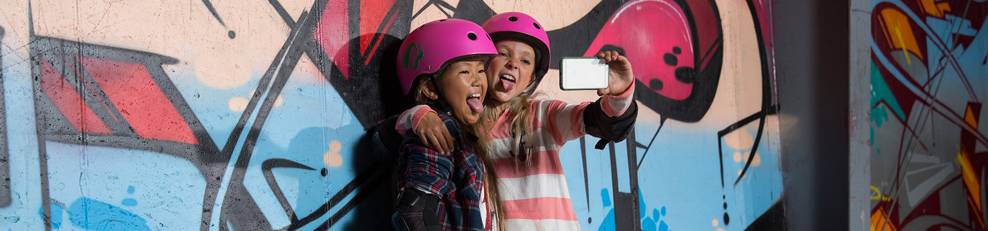  two skater girls taking a selfie in front of a graffiti backdrop 