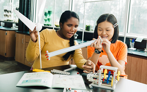 two girls working on building a robot at a table