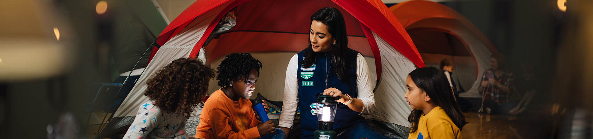  three young girl scouts sitting in front of a tent with their girl scout leader 