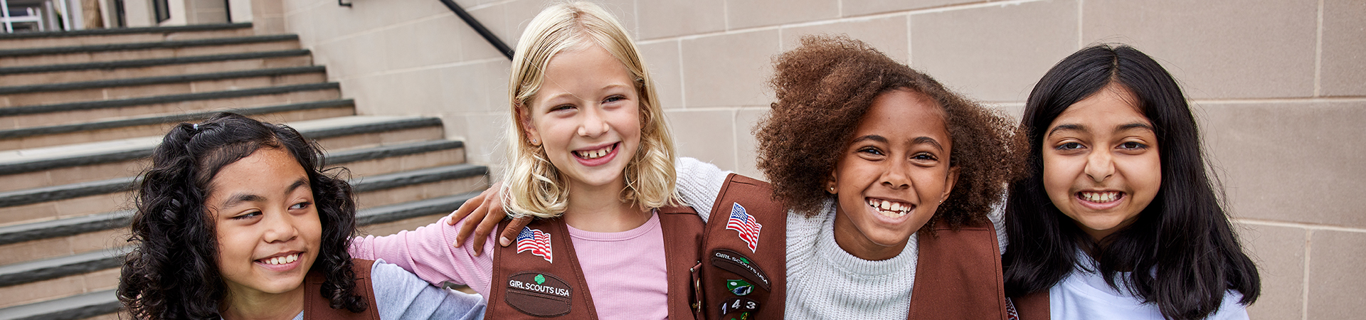  four brownie girl scouts smiling at the camera with their arms around each other's shoulders 
