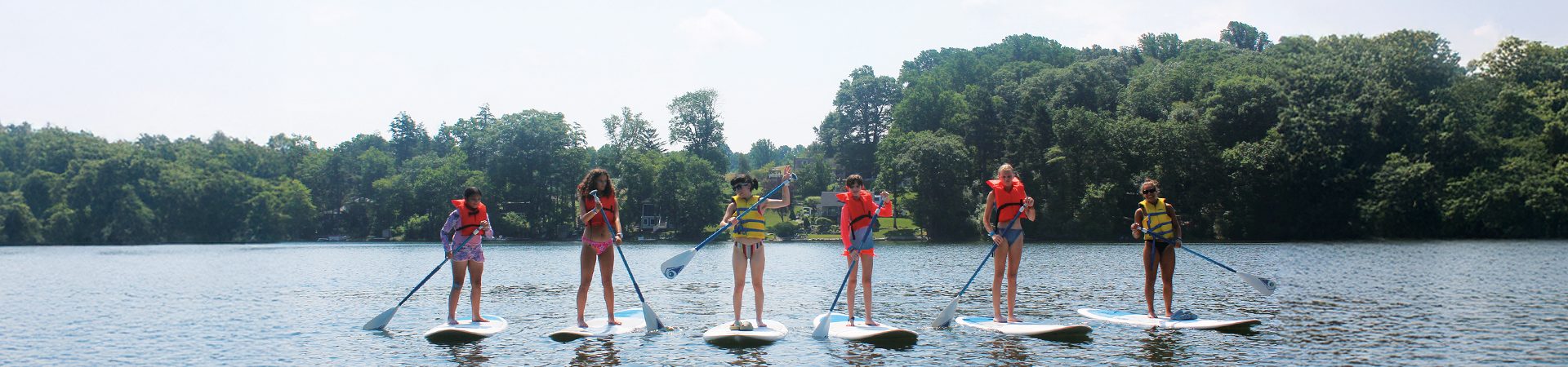  three sailboats and a kayak on a lake with green trees as a backdrop 
