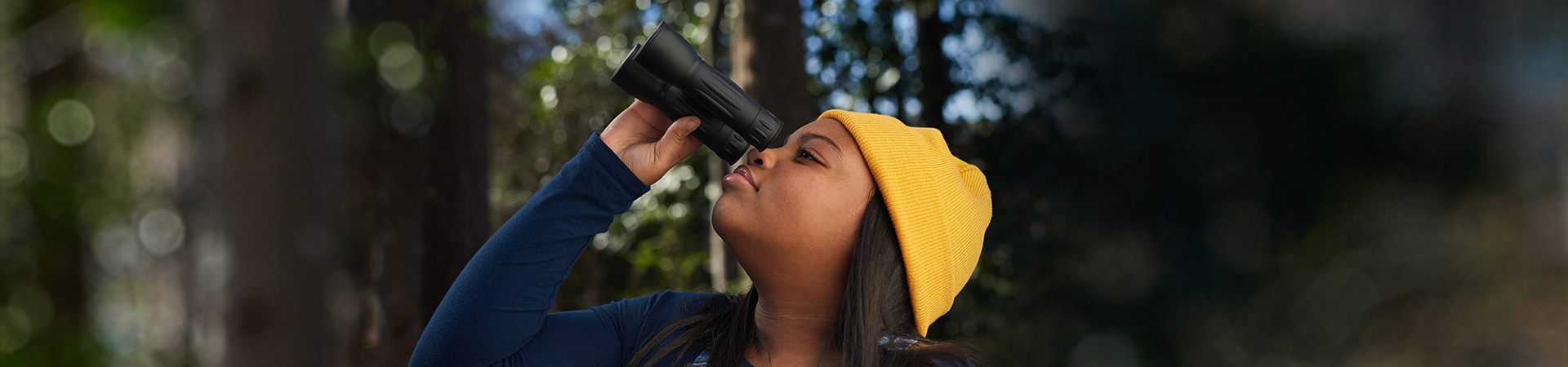  black high school girl wearing yellow beanie knitted hat holding binoculars outside in woods 