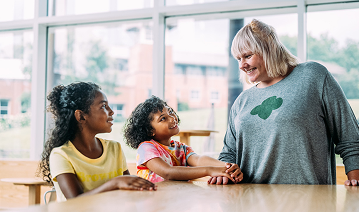 A troop leader  talking with two Girl Scouts