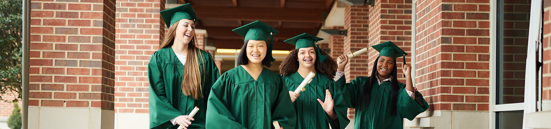  four high school graduates in green cap and gown carrying diplomas 